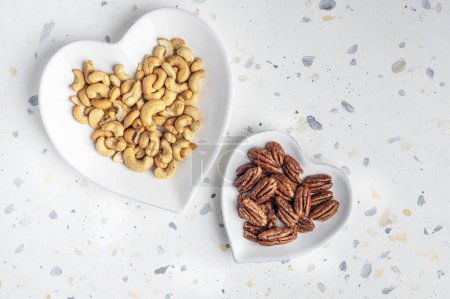 Photo for Cashews and pecans in heart-shaped plates. Top view. Place for text - Royalty Free Image