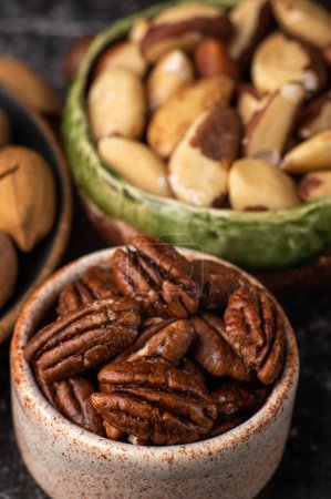 Photo for Nuts mix in ceramic plates on black table. Brazil nut shelled, pecan shelled, pecan nut in shell - Royalty Free Image