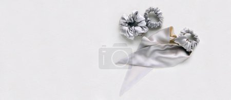 Photo for Silk silver ribbon and scrunchy on white flat lay. bobbles and scarf with hairdressing tools and accessories. Scrunchies, Elastic Hair Bands, Bobble Sports Hairband. white banner - Royalty Free Image
