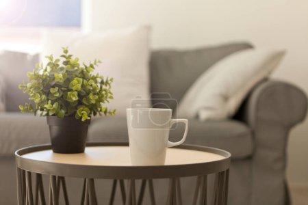 Foto de Taza de té caliente. taza blanca en la mesa cerca de acogedor sofá gris. almohadas y manta. Inicio relajante estilo de vida. Luz solar en una habitación - Imagen libre de derechos
