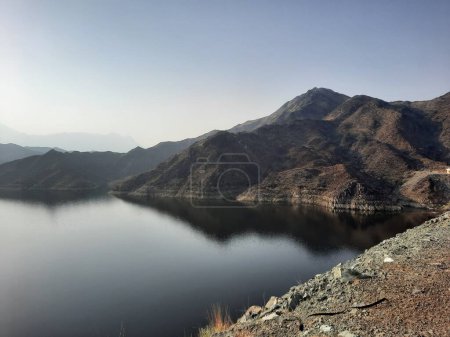 Téléchargez les photos : Une belle vue de jour sur le barrage de Wadi Qanuna à Al Bahah, en Arabie Saoudite. L'eau du barrage et les collines environnantes présentent une belle scène au soleil. - en image libre de droit