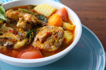 Téléchargez les photos : Photo rapprochée d'une portion de soupe spéciale indonésienne à la queue de bœuf, servie dans un bol et une nappe bleue - en image libre de droit