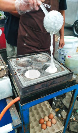 Photo for Serabi dough made from rice flour is being poured onto the grill. Serabi is a street snack from Indonesia. Generally there are two variants of Serabi, namely savory and sweet - Royalty Free Image