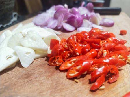 Sliced red chilies, shallots and garlic on a cutting board in preparation for cooking