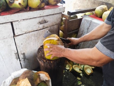 The coconuts are being split to be peeled and taken water and flesh using a cleaver by the coconut seller