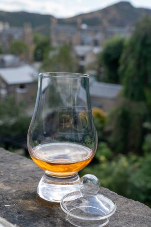 Foto de Glass of single malt scotch whisky served on old window sill in Scottisch house with view on old part of Edinburgh city, Scotland, UK, dram of blended whiskey - Imagen libre de derechos
