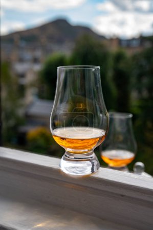 Foto de Glass of single malt scotch whisky served on old window sill in Scottisch house with view on old part of Edinburgh city, Scotland, UK, dram of blended whiskey - Imagen libre de derechos