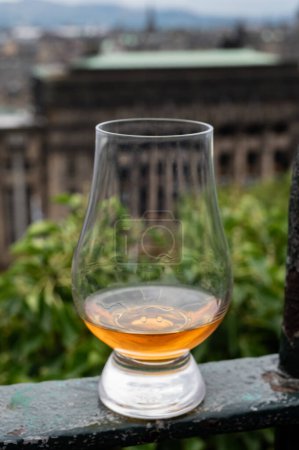 Foto de Glass of single malt scotch whisky and view from Calton hill to park and old parts of Edinburgh city in rainy summer day, Scotland, UK - Imagen libre de derechos