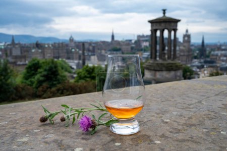 Foto de Copa Dram de whisky escocés de malta simple y vista desde la colina de Calton hasta el parque y las partes antiguas de la ciudad de Edimburgo en el lluvioso día de verano, Escocia, Reino Unido - Imagen libre de derechos