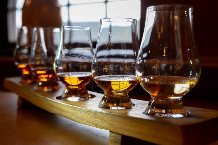Foto de Flight of single malt scotch whisky in glasses served in bar in Edinburgh, UK, tasting of dram of whiskey - Imagen libre de derechos