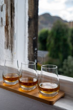 Foto de Flight of single malt scotch whisky served on old window sill in Scottisch house with view on old part of Edinburgh city, Scotland, UK, dram of whiskey - Imagen libre de derechos