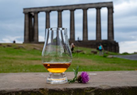 Foto de Copa Dram de whisky escocés de malta simple y vista desde la colina de Calton hasta el parque y las partes antiguas de la ciudad de Edimburgo en el lluvioso día de verano, Escocia, Reino Unido - Imagen libre de derechos