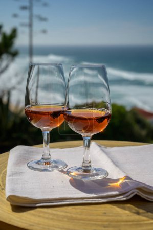 Tasting of sweet moscatel de setubal or porto portuguese wine and view on sunny blue Atlantic ocean near Sintra in Lisbon area, Portugal