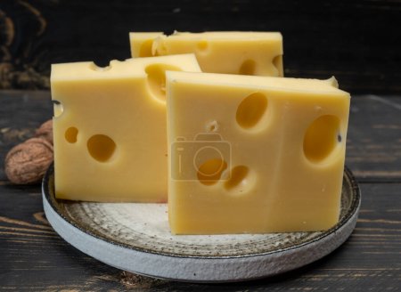 Block of Swiss medium-hard yellow cheese emmental or emmentaler with round holes and cheese knife close up