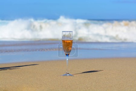Téléchargez les photos : One glass of rose champagne or cava sparkling wine served on white sandy tropical beach and blue ocean water, romantic vacation, winter sun on Fuerteventura, Canary, Spain - en image libre de droit