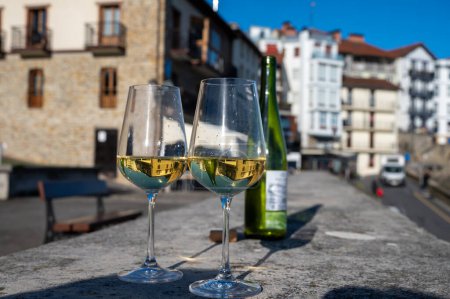 Téléchargez les photos : Tasting of txakoli or chacoli slightly sparkling very dry white wine produced in Spanish Basque Country with view on old port and sunny village Getaria, Spain - en image libre de droit