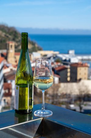 Téléchargez les photos : Tasting of txakoli or chacol slightly sparkling very dry white wine produced in Spanish Basque Country with view on port and sunny village Getaria, Spain - en image libre de droit