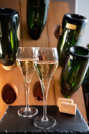 Copas de vino blanco espumoso champán gran cru o cava con burbujas y clásico estante de madera pupitre champán con botellas vacías en el fondo