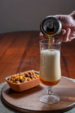 Foto de Verter cerveza de trigo alemana es vidrio y un tazón con nueces de mezcla de fiesta, de cerca - Imagen libre de derechos