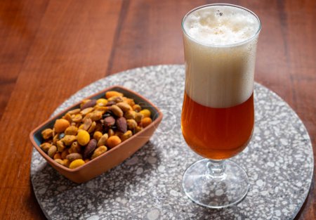 Photo for Glass of Belgian light blond beer made in abbey and bowl with party mix nuts, close up - Royalty Free Image
