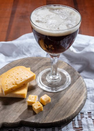 Foto de Vaso de cerveza marrón abadía belga y tabla de madera con queso belga antiguo hecho por los monjes de leche de vaca, los gustos de Bélgica - Imagen libre de derechos