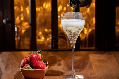 Téléchargez les photos : Verre de champagne brut bulles vin en verre de tulipe et petit bol avec des fraises fraîches sur fond de lumières de bar du soir - en image libre de droit