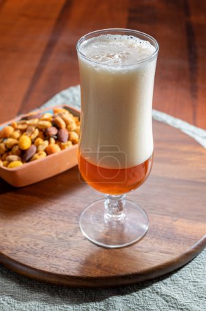 Foto de Verter cerveza de trigo alemana es vidrio y un tazón con nueces de mezcla de fiesta, de cerca - Imagen libre de derechos