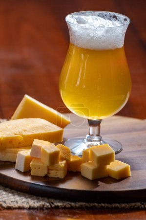 Photo for Glass of Belgian light blonde beer made in abbey and wooden board with variety of belgian cheeses, food and beer pairing - Royalty Free Image