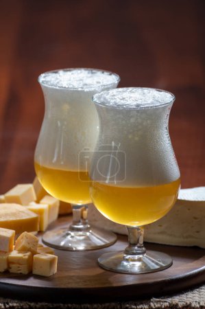 Photo for Glasses of Belgian light blonde beer made in abbey and wooden board with variety of belgian cheeses, food and beer pairing - Royalty Free Image