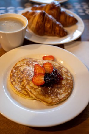 Photo for Breakfast with homemade American pancakes served with strawberry jam and fresh ripe strawberries, coffee and croissants - Royalty Free Image