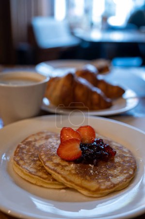 Photo for Breakfast with homemade American pancakes served with strawberry jam and fresh ripe strawberries, coffee and croissants - Royalty Free Image
