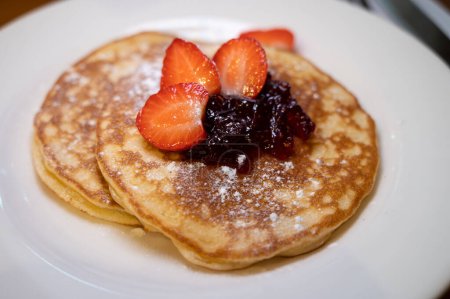 Photo for Homemade American pancakes served with strawberry jam and fresh ripe strawberries on a white board, sweet dessert, close up - Royalty Free Image