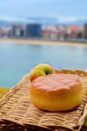 Téléchargez les photos : Fromage de vache fumé dur espagnol de Pria, Asturies, servi en plein air avec vue sur la plage de San Lorenzo et la promenade de Gijon - en image libre de droit