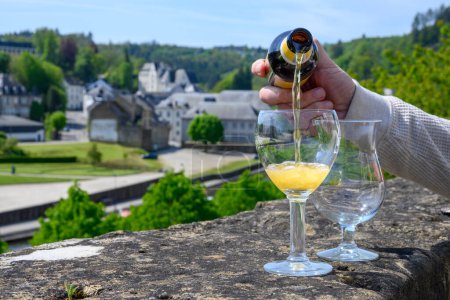 Pouring of blond strong Belgian abbey beer in to glass in sunny summer day with nice view on old town Bouillon, Belgium