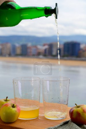 Gießen von natürlichen asturischen Apfelwein aus fermentierten Äpfeln in Holzfässern sollte aus großer Höhe für Luftblasen in das Getränk und Blick auf San Lorenzo Strand von Gijon gegossen werden