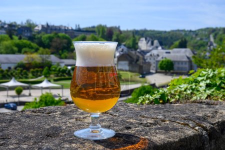 Ein Glas blondes, starkes belgisches Abteibier auf der alten Burgmauer an einem sonnigen Sommertag mit schönem Blick auf die Altstadt Bouillon, Belgien