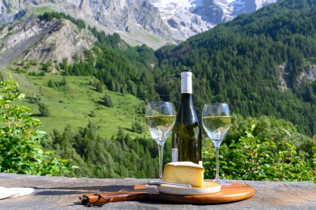 Téléchargez les photos : Fromage et vin, verres de vin blanc sec Roussette de Savoie et Vin de Savoie de Savoie avec tomme et vue sur les Hautes Alpes avec neige au sommet en été. - en image libre de droit