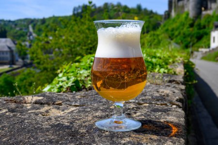 Photo for Glass of blond strong Belgian abbey beer on old castle wall in sunny summer day with nice view on old town Bouillon, Belgium - Royalty Free Image