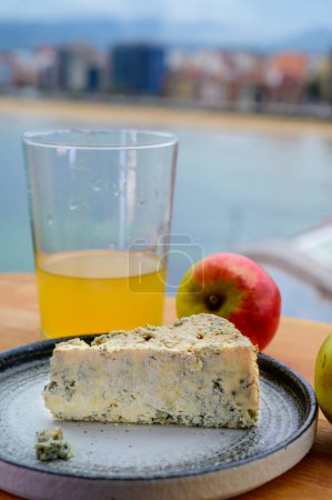 Foto de Comida y bebida asturiana, queso cabrales de vaca azul de Arenas servido al aire libre con un vaso de sidra de manzana natural y vista de la playa de San Lorenzo en Gijón, España - Imagen libre de derechos