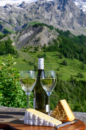 Foto de Queso y vino, vasos de vino blanco seco Roussette de Savoie y Vin de Savoie de la región de Saboya con queso tomme y vista de las montañas de Hautes Alpes con nieve en la parte superior - Imagen libre de derechos
