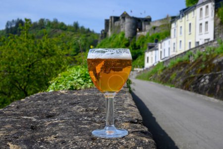 Photo for Glass of blond strong Belgian abbey beer on old castle wall in sunny summer day with nice view on old town Bouillon, Belgium - Royalty Free Image