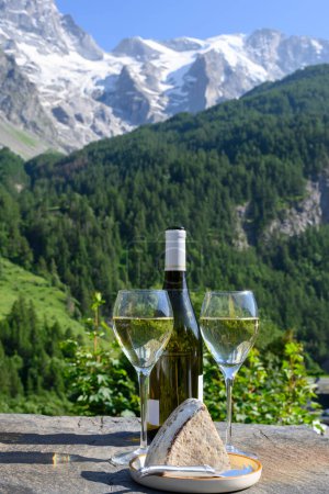 Foto de Queso y vino, vasos de vino blanco seco Roussette de Savoie y Vin de Savoie de la región de Saboya con queso tomme y vista de las montañas de Hautes Alpes con nieve en la parte superior - Imagen libre de derechos