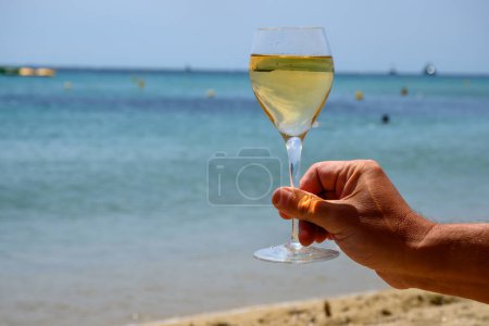 Téléchargez les photos : Heure d'été en Provence, verre de vin blanc froid sur la plage de sable de Pampelonne près de Saint-Tropez par temps ensoleillé, département du Var, France. - en image libre de droit