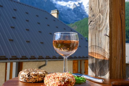 Téléchargez les photos : Fromage et vin, verre de vin de rose sec et fromages de chèvre frais avec garnitures au poivre, vue sur les Hautes Alpes avec neige sur le dessus - en image libre de droit