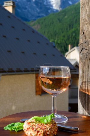 Téléchargez les photos : Fromage et vin, verre de vin de rose sec et fromages de chèvre frais avec garnitures au poivre, vue sur les Hautes Alpes avec neige sur le dessus - en image libre de droit