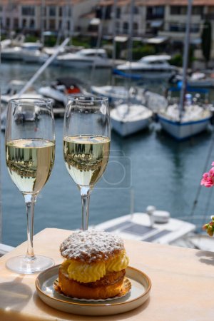 Drinking of French brut champagne sparkling wine with cake Tarte Tropezienne, club party in yacht harbour of Port Grimaud near Saint-Tropez, French Riviera vacation, Var, France