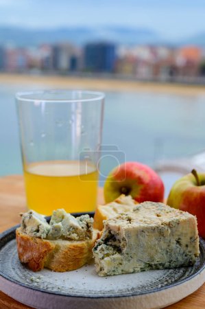Téléchargez les photos : Accompagnement alimentaire dans les Asturies, fromage cabrales de vache bleue des grottes dans Arenas servi en plein air avec verre de cidre de pomme naturel et vue sur la plage de San Lorenzo à Gijon, Espagne - en image libre de droit