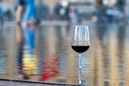 Photo for Tasting of Bordeaux blended red wine with wine city Bordeaux on background, left bank of Gironde Estuary, France. Glass of red French wine served outdoor. - Royalty Free Image
