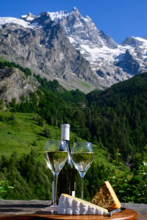 Téléchargez les photos : Fromage et vin, verres de vin blanc sec Roussette de Savoie et Vin de Savoie de Savoie, tomme et fromage bleu, vue sur les Hautes Alpes avec neige au sommet en été. - en image libre de droit