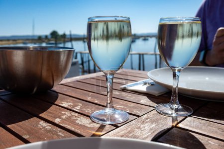 Photo for Drinking of white wine at farm cafe in oyster-farming village, with view on boats and water of Arcachon bay, Cap Ferret peninsula, Bordeaux, France in sunny day - Royalty Free Image